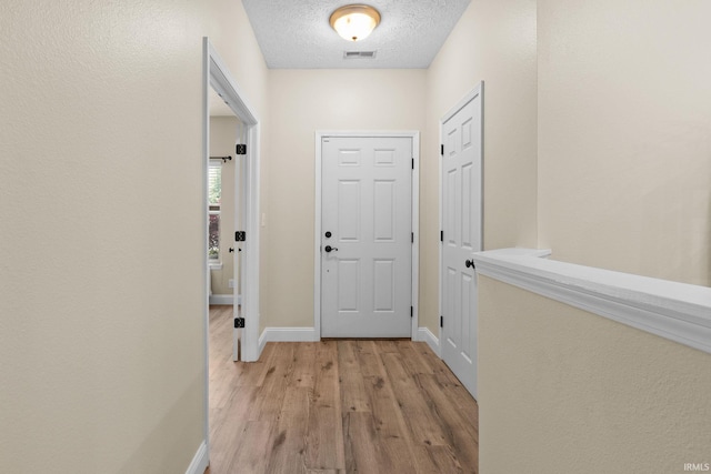 doorway featuring light wood finished floors, baseboards, and a textured ceiling