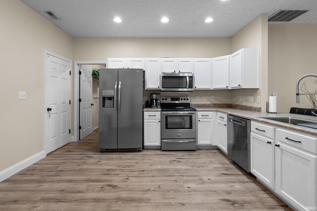 kitchen with stainless steel appliances, a sink, light wood-type flooring, white cabinets, and recessed lighting