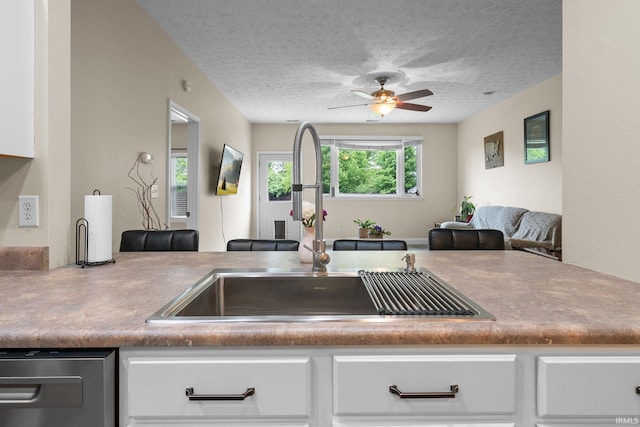 kitchen featuring a sink, a ceiling fan, white cabinets, a textured ceiling, and stainless steel dishwasher