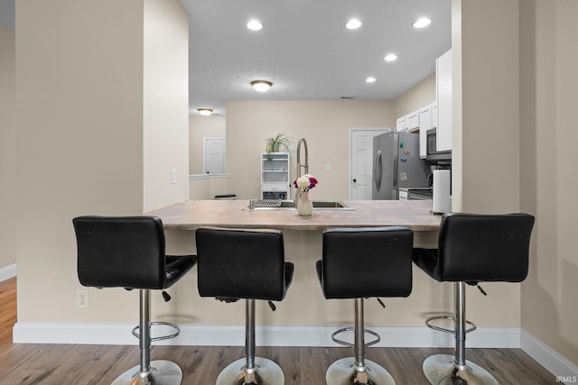 kitchen featuring a peninsula, dark wood-type flooring, appliances with stainless steel finishes, a kitchen bar, and recessed lighting