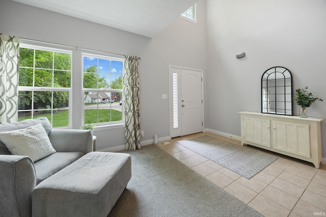 foyer featuring light tile patterned floors, baseboards, a towering ceiling, and light colored carpet