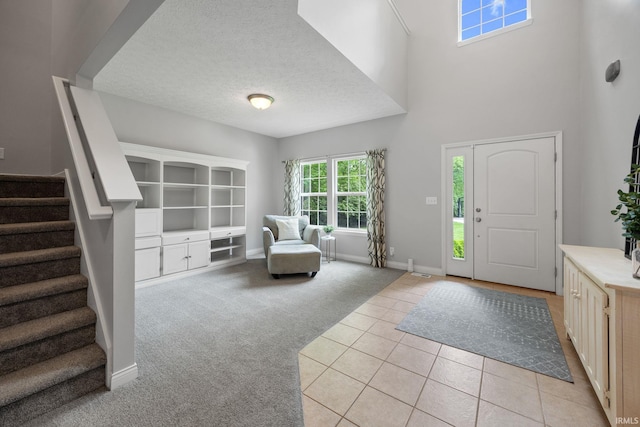 entrance foyer with stairs, baseboards, light carpet, light tile patterned floors, and a textured ceiling