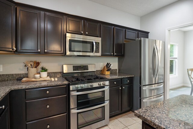 kitchen with stainless steel appliances, dark brown cabinets, dark stone countertops, and light tile patterned floors