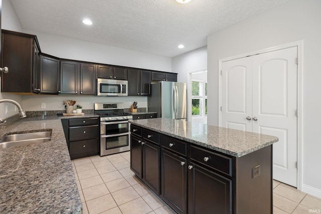 kitchen with appliances with stainless steel finishes, a sink, light tile patterned floors, a center island, and dark stone countertops