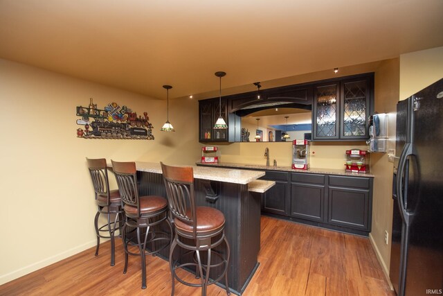 indoor wet bar with black fridge with ice dispenser, wood finished floors, baseboards, and hanging light fixtures