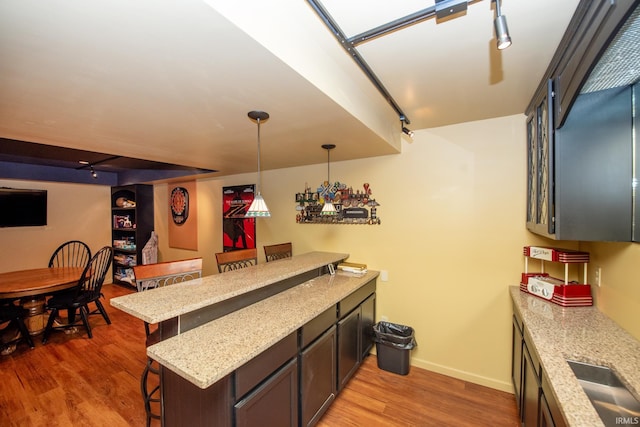 kitchen with a kitchen breakfast bar, light wood-type flooring, baseboards, hanging light fixtures, and light stone counters