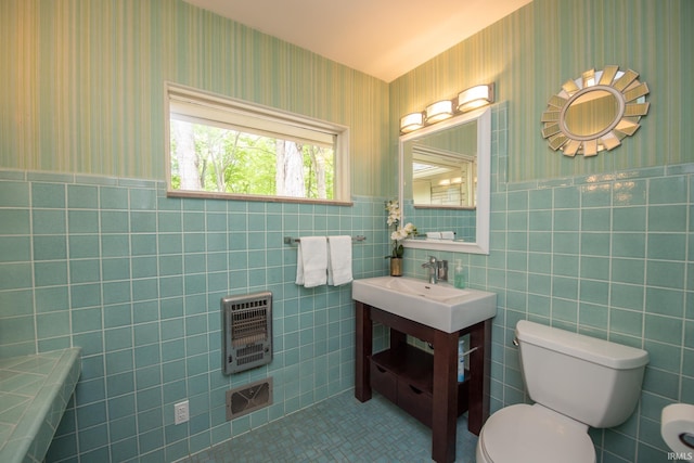bathroom featuring heating unit, toilet, wallpapered walls, tile walls, and wainscoting