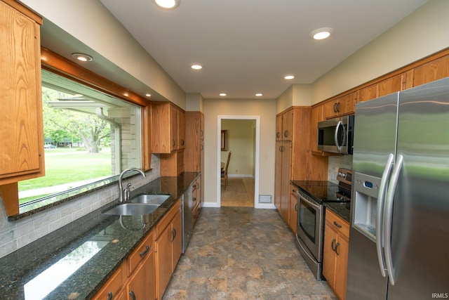 kitchen with appliances with stainless steel finishes, a sink, brown cabinetry, backsplash, and stone finish floors
