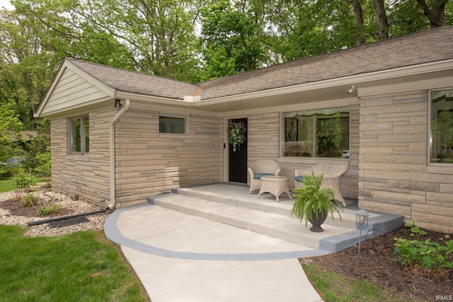 entrance to property featuring stone siding and roof with shingles