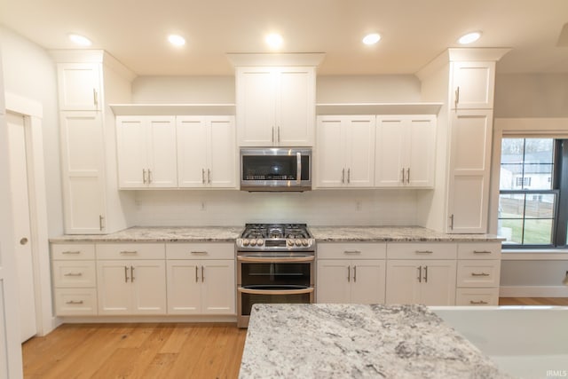 735 E Holland Dr, Bloomington, IN 47401 - kitchen featuring stainless steel appliances, white cabinetry, light wood-style floors, backsplash, and light stone counters
