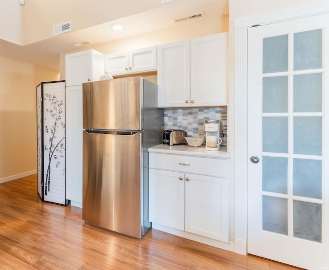 kitchen with freestanding refrigerator, white cabinetry, and tasteful backsplash