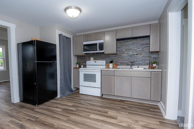 kitchen with freestanding refrigerator, stainless steel microwave, white electric range oven, a sink, and wood finished floors