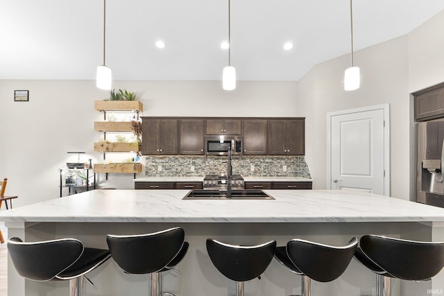 7689 Accio Cv, Fort Wayne, IN 46835 - kitchen with stainless steel microwave, backsplash, dark brown cabinetry, a kitchen island with sink, and a breakfast bar area