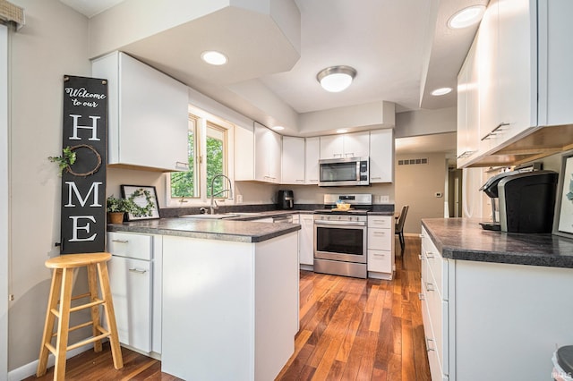 kitchen with appliances with stainless steel finishes, a sink, a peninsula, hardwood / wood-style flooring, and white cabinetry