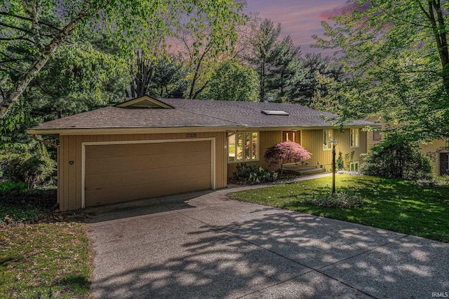 ranch-style home featuring a garage, driveway, a lawn, and a shingled roof