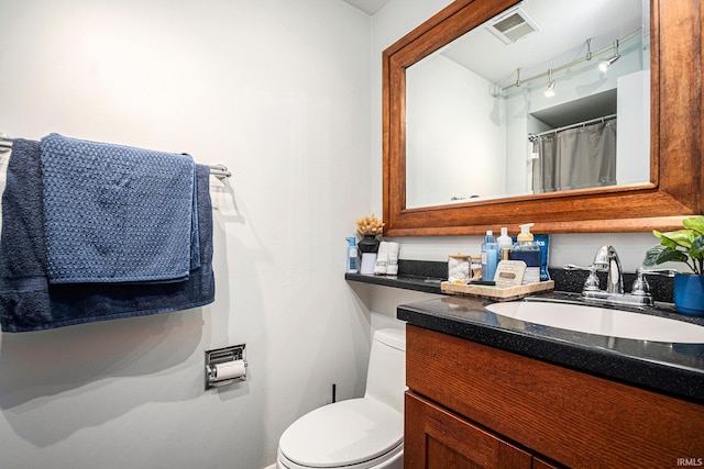 bathroom featuring toilet, vanity, rail lighting, and baseboards