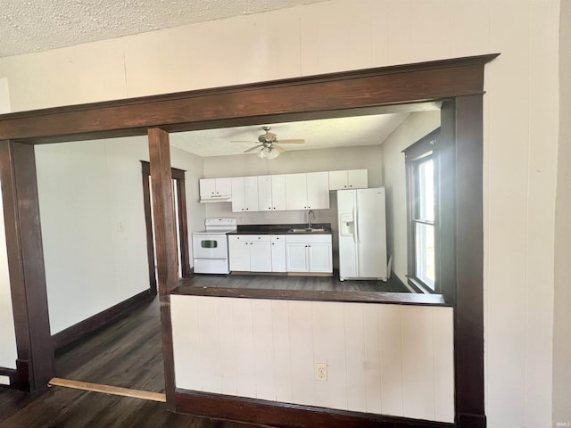 kitchen with white appliances, a sink, dark wood-style floors, dark countertops, and white cabinets