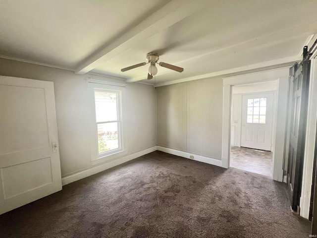 unfurnished room featuring dark carpet, a ceiling fan, beamed ceiling, a barn door, and baseboards