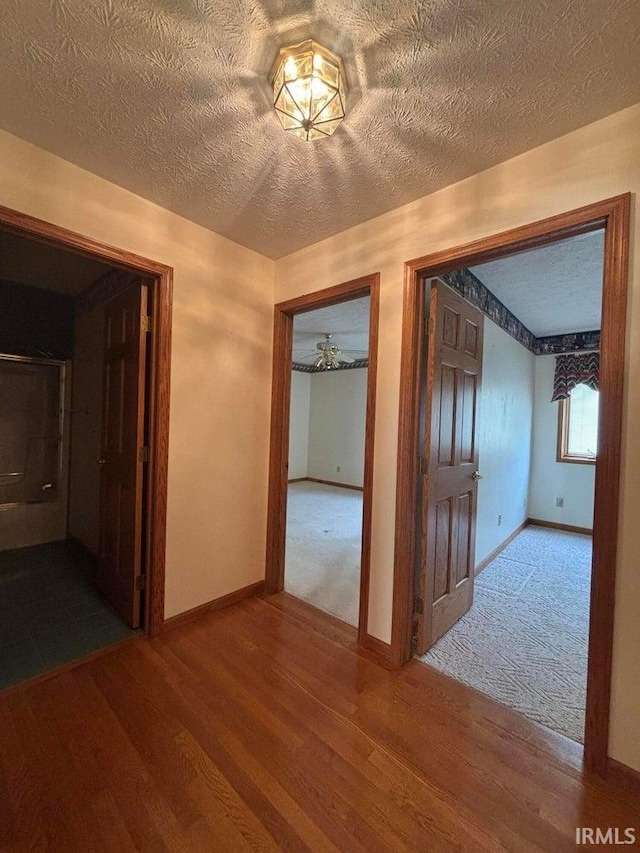 hallway featuring wood finished floors, baseboards, and a textured ceiling