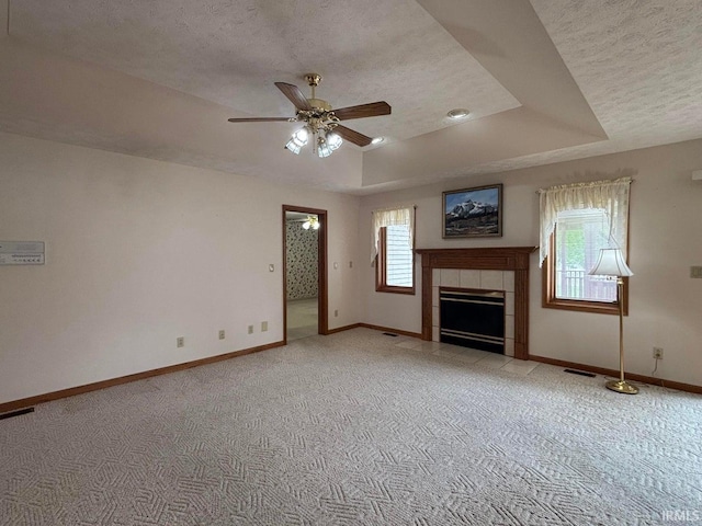unfurnished living room featuring a textured ceiling, a ceiling fan, light carpet, a tray ceiling, and baseboards