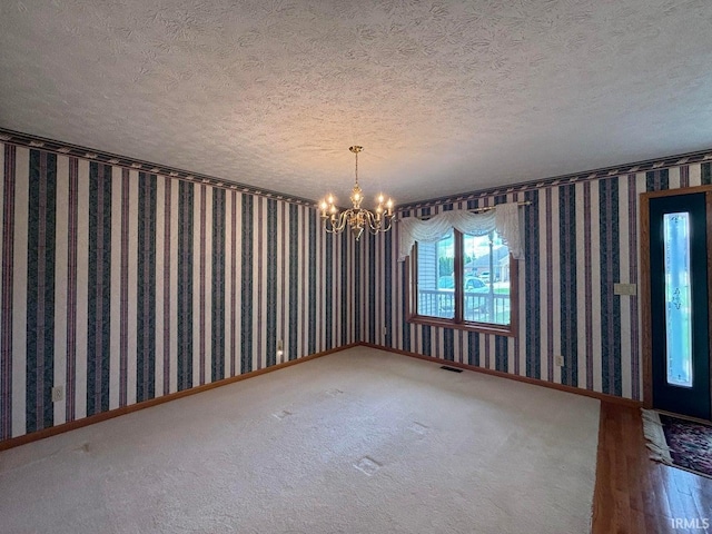 empty room with a chandelier, a textured ceiling, wallpapered walls, and baseboards
