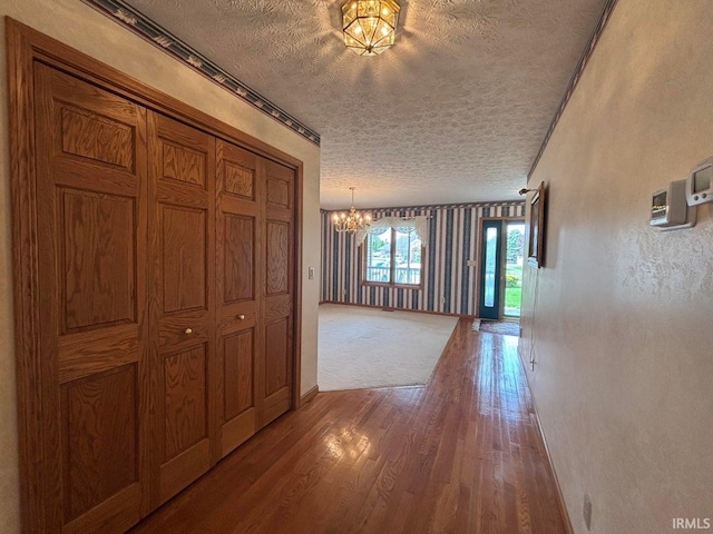 corridor with a textured ceiling, a chandelier, wood finished floors, and baseboards