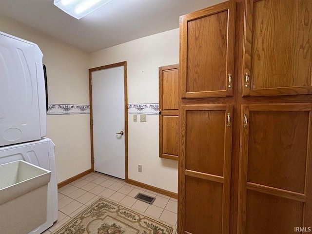 laundry area with estacked washer and dryer, light tile patterned floors, baseboards, and cabinet space