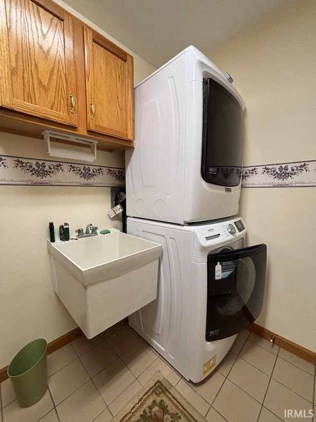 laundry room with stacked washing machine and dryer, light tile patterned flooring, cabinet space, and baseboards