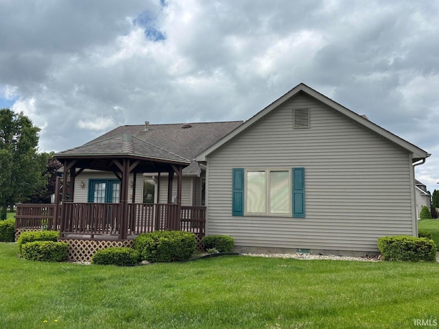 back of property featuring a yard, a deck, and roof with shingles