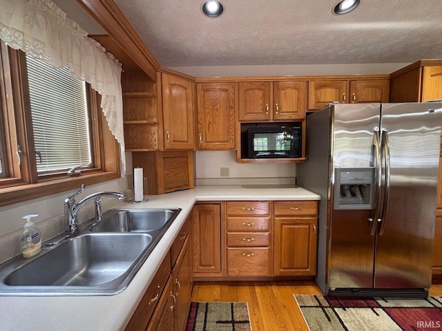 kitchen with stainless steel fridge with ice dispenser, black microwave, a sink, brown cabinets, and light wood-type flooring