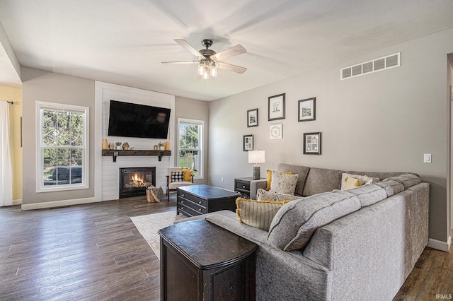 living area featuring a ceiling fan, a fireplace, dark wood-style floors, and plenty of natural light