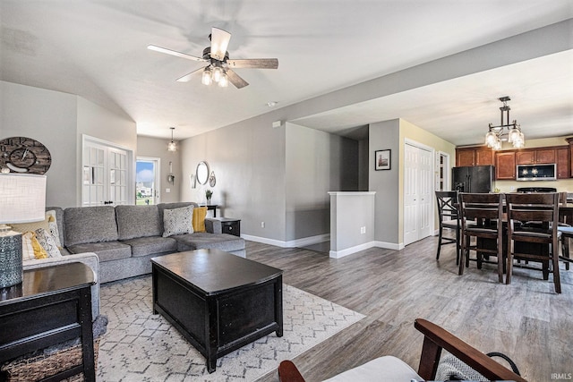 living room with light wood finished floors, a chandelier, a ceiling fan, and baseboards