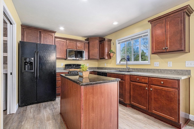 kitchen featuring black refrigerator with ice dispenser, stainless steel microwave, a sink, light wood-style flooring, and range