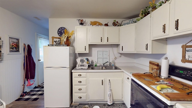 kitchen featuring freestanding refrigerator, a sink, light countertops, range, and white cabinetry