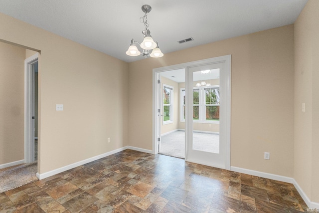 unfurnished room featuring stone tile floors, a chandelier, and baseboards
