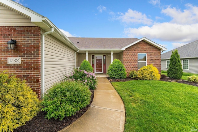 view of exterior entry with a yard and brick siding