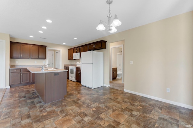 kitchen with white appliances, stone tile flooring, light countertops, baseboards, and a center island with sink