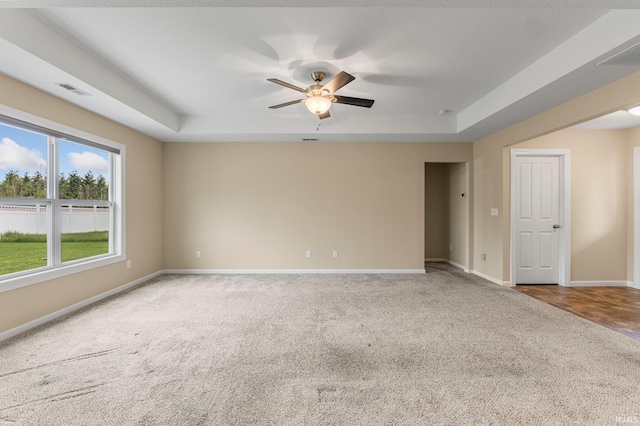 carpeted spare room featuring a raised ceiling, ceiling fan, and baseboards
