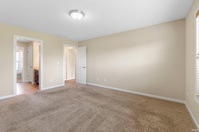 unfurnished bedroom featuring light carpet, baseboards, and ensuite bath