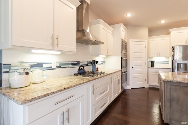 kitchen with wall chimney range hood, stainless steel appliances, white cabinets, dark wood-style floors, and tasteful backsplash