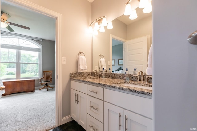ensuite bathroom featuring double vanity, ceiling fan, and baseboards