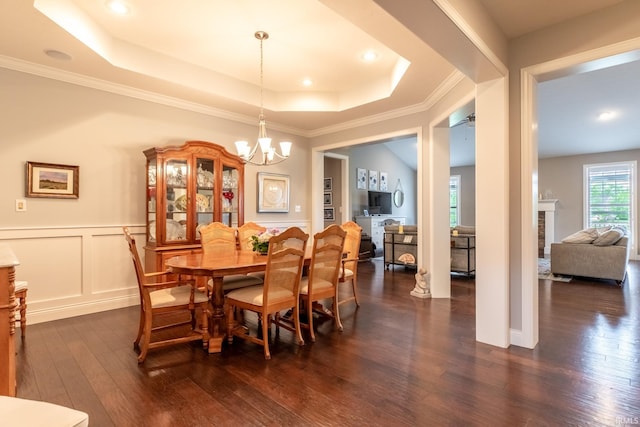 dining space with dark wood-style floors, a chandelier, a raised ceiling, ornamental molding, and wainscoting