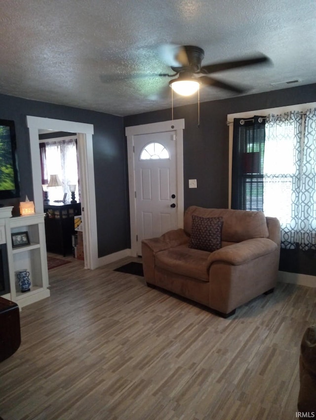 living area featuring wood finished floors, a ceiling fan, a textured ceiling, and baseboards