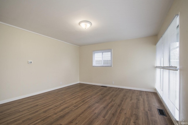empty room with dark wood finished floors, baseboards, and crown molding