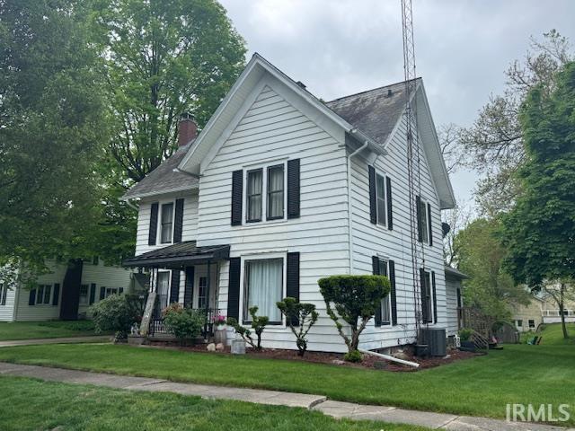 view of front of home featuring a chimney, a front yard, cooling unit, a shingled roof, and a porch