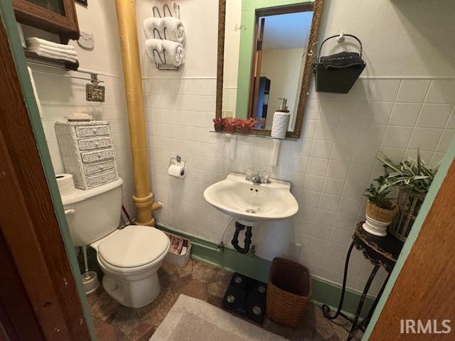 half bath featuring tile walls, toilet, and a sink