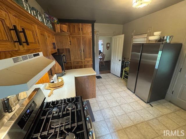 kitchen featuring freestanding refrigerator, light countertops, brown cabinetry, and range with gas cooktop