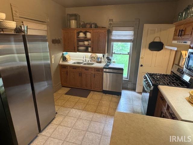 kitchen featuring stainless steel appliances, a sink, brown cabinetry, light countertops, and open shelves
