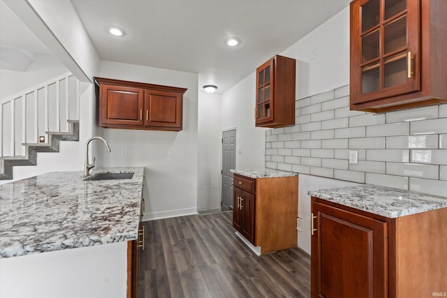 kitchen with a sink, light stone countertops, dark wood finished floors, decorative backsplash, and glass insert cabinets