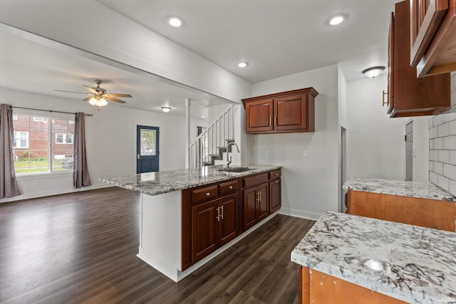 kitchen with a sink, a peninsula, dark wood-style flooring, baseboards, and ceiling fan